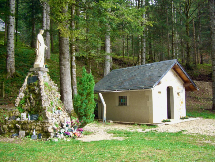 Petite maison blanche dans une clairière boisée.